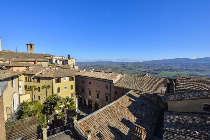 Panoramic view of Todi's historic center, featuring terracotta-roofed buildings and hills in the background.