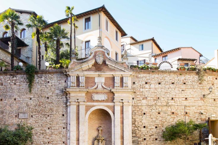 Historic building with fountain, surrounded by greenery and ancient walls, in a characteristic setting of Todi.