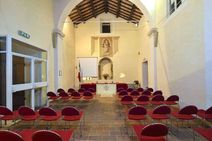 Interior of an event hall with neatly arranged red chairs. The atmosphere is warm and inviting.