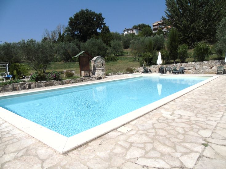 Une piscine nichée dans la campagne ombrienne, entourée d'arbres verdoyants et de champs.
