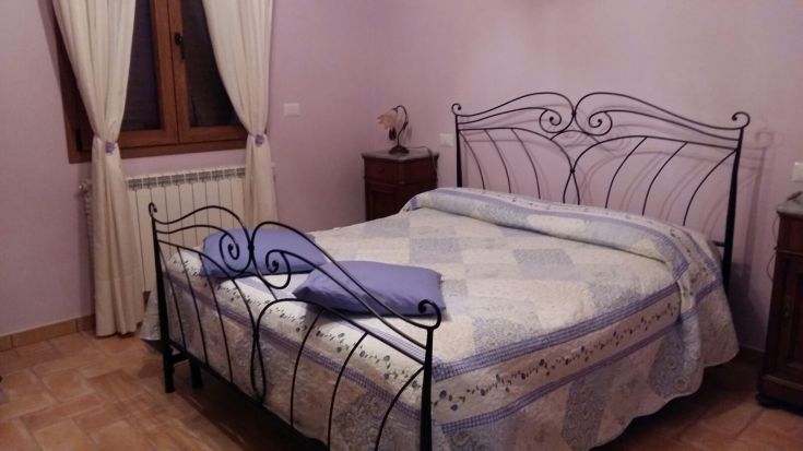 Chambre simple et accueillante avec un lit double en fer forgé et des murs lilas.