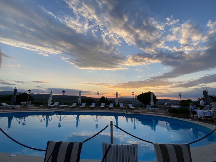 A sunset view of a pool surrounded by greenery, featuring colorful clouds and a tranquil atmosphere.