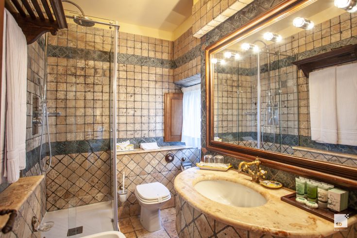 A bathroom featuring stone and terracotta details, with a marble shower and sink.