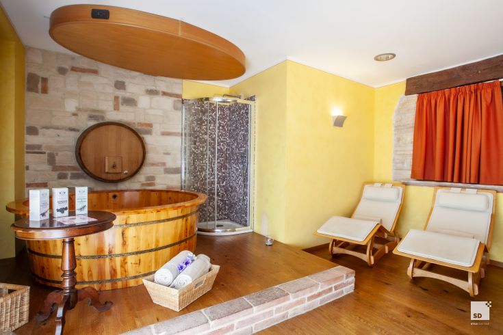 A cozy wellness center featuring a wooden hot tub, contemporary shower, and loungers, ideal for relaxation.