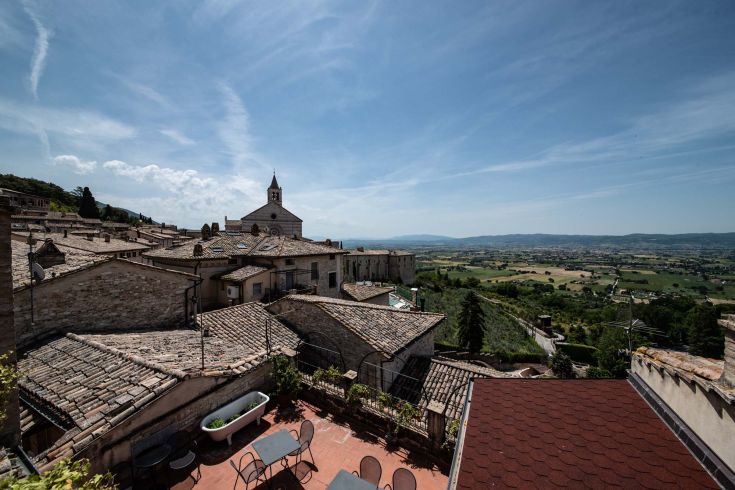 Panorama di Assisi con tetti in stile medievale e campanile visibile sullo sfondo.