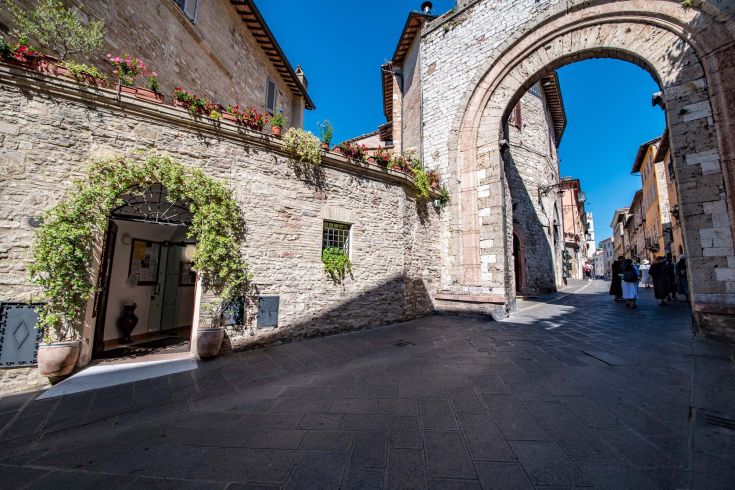Un angolo del centro storico con archi, edifici in pietra e un camino decorato con fiori.