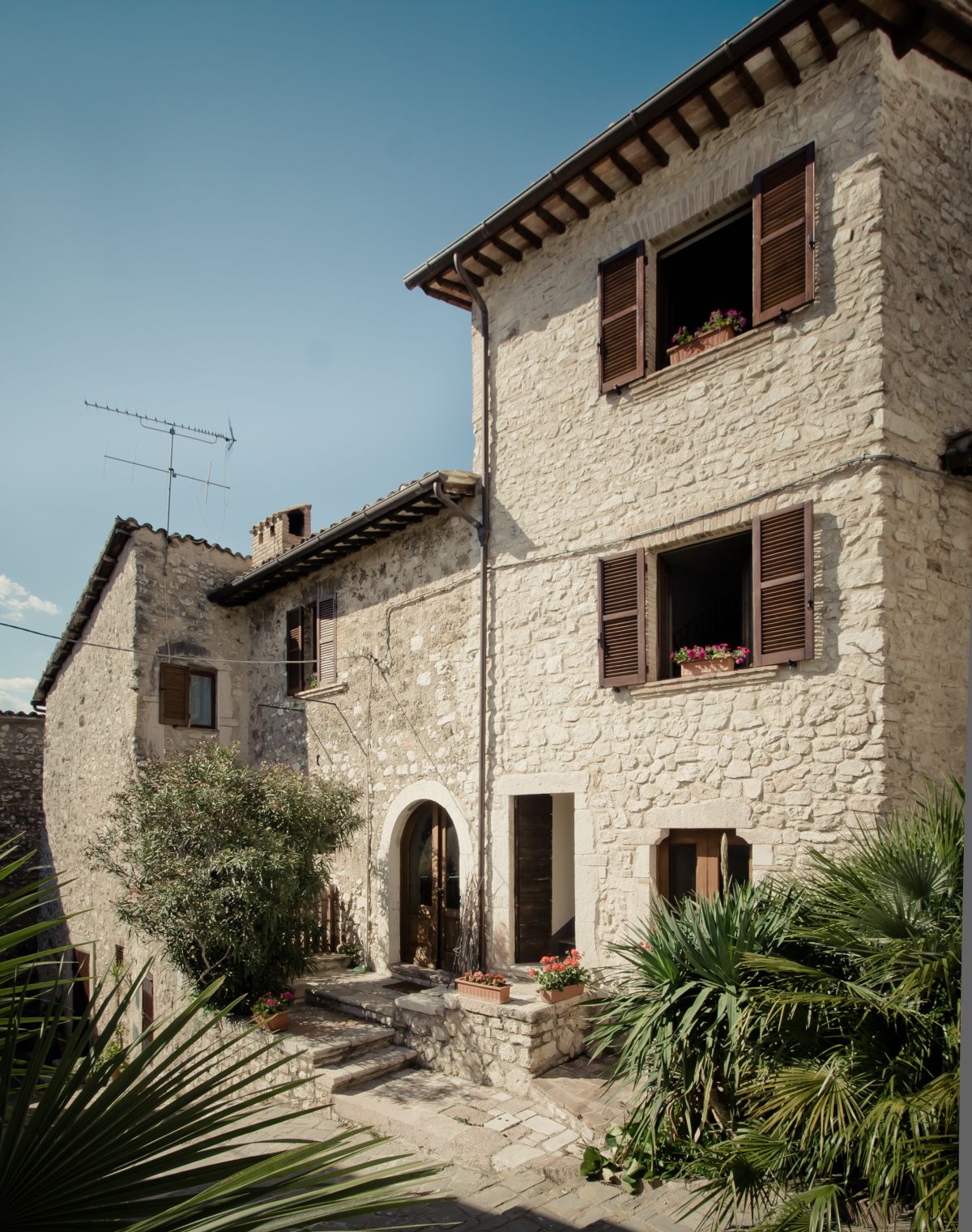 The image shows a stone building with window plants, surrounded by natural scenery.