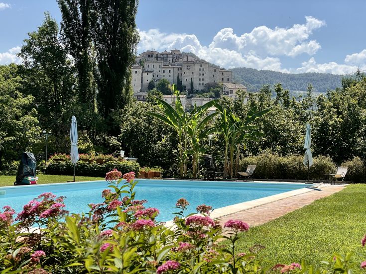 Ein Pool umgeben von üppigem Grün und Blumen, mit einem historischen Gebäude im Hintergrund.