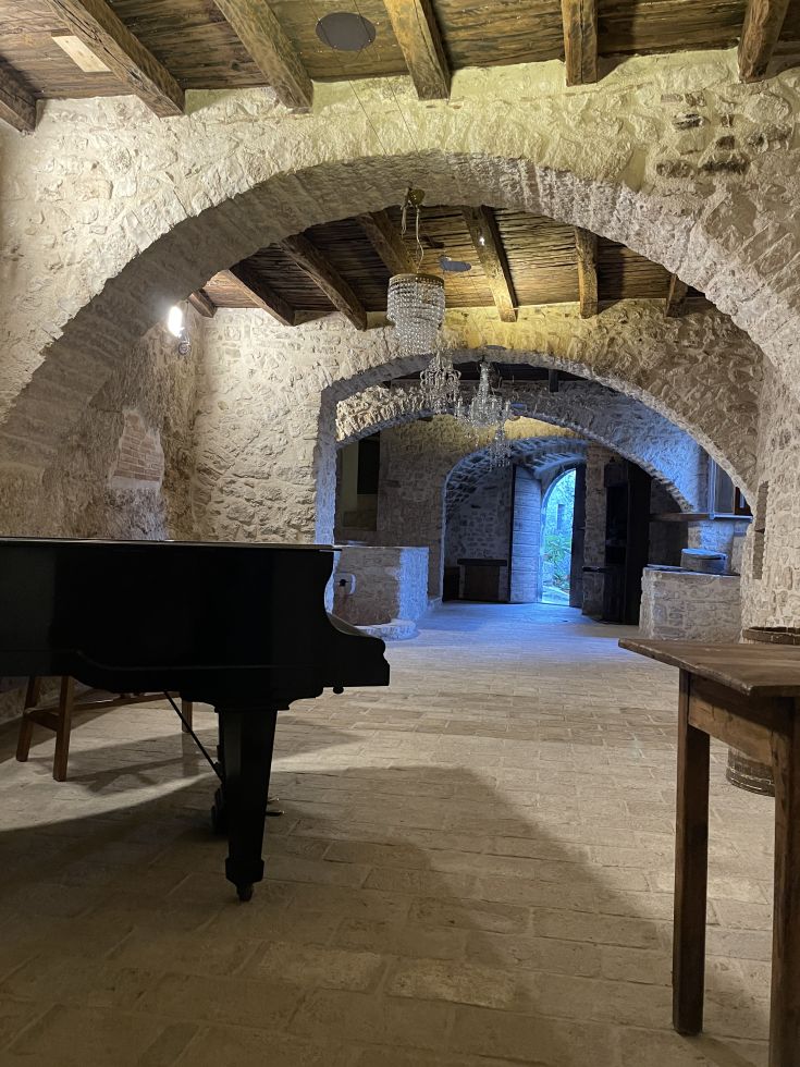 Innenansicht eines Steinpalastes mit einem Klavier, hellen Holzbalken und sanfter Beleuchtung.
