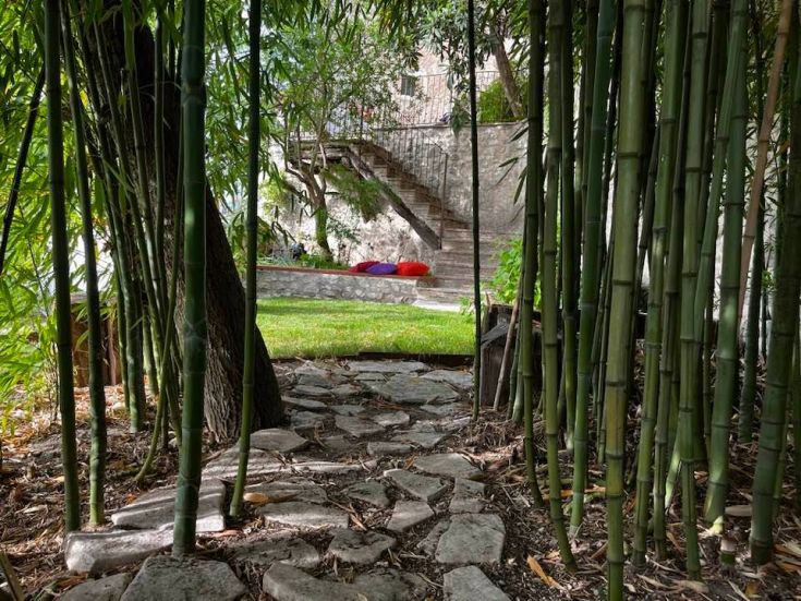 Ein Steinweg schlängelt sich durch einen Bambuswald und führt zu einem gepflegten grünen Garten.