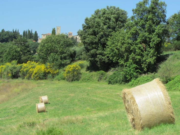 A serene countryside landscape featuring hay bales and a medieval building in the background.