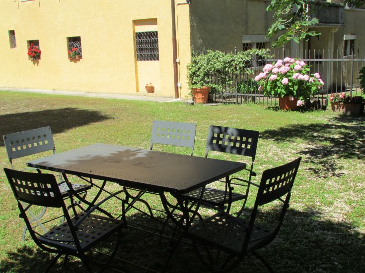 An outdoor area with a table and chairs, surrounded by lush greenery.