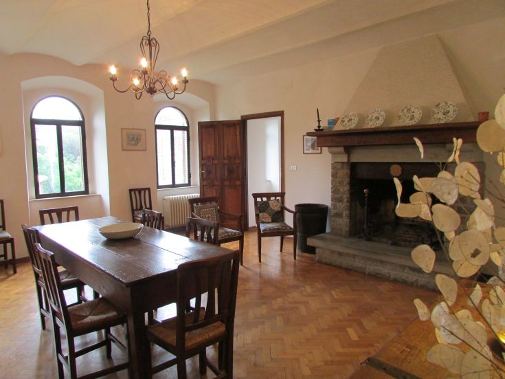 Cozy interior of a farmhouse with a wooden table, chairs, and a fireplace, ideal for meals and relaxation.