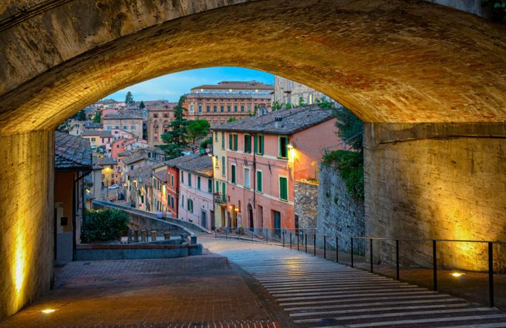 Scena di una strada storica in una città umbra, con edifici colorati e un cielo limpido.