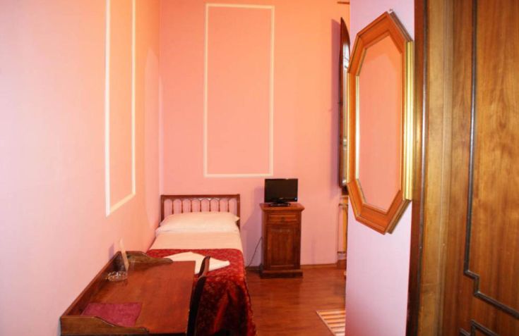 Camera in stile Liberty con decorazioni rosa, scrivania e TV posizionata su un mobile.