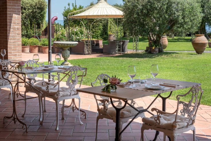 Freiluftrestaurant mit Schmiedeeisentischen, eingebettet in eine gepflegte grüne Umgebung.