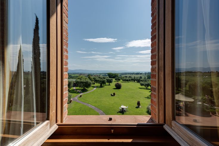 Eine friedliche Szene vom Fenster aus, die einen gut gepflegten Garten und grüne Hügel in der Ferne zeigt.