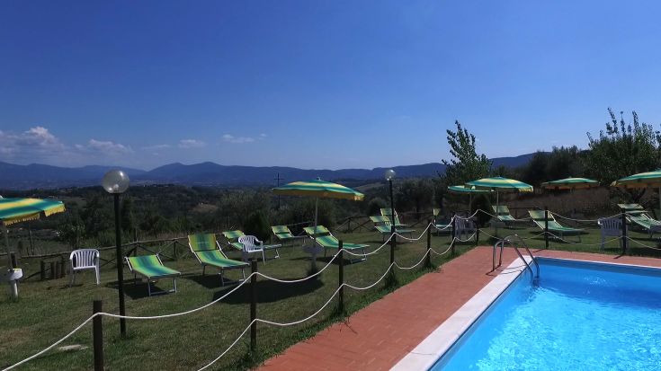Piscina contornata da lettini e ombrelloni, con vista sulle colline della zona umbra.