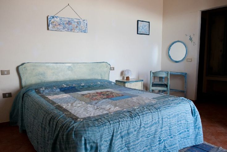 Camera matrimoniale semplice con pareti blu, arredamento sobrio e luce naturale che illumina l'ambiente.