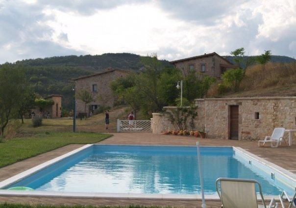 Ein Pool, der in einer natürlichen Umgebung liegt, umgeben von rustikalen Gebäuden und sanften grünen Hügeln.