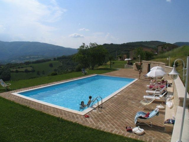 Una piscina naturale situata in un contesto verde, circondata da dolci colline.
