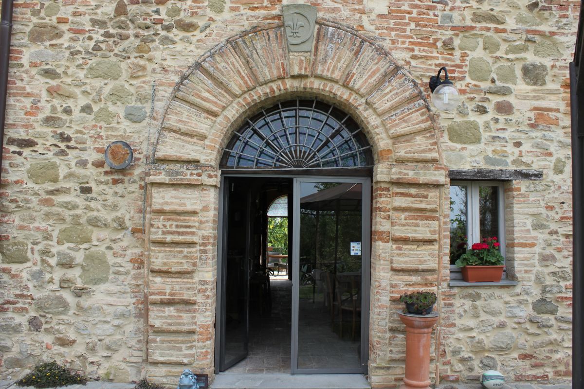 Entrée d'un bâtiment en pierre avec des arcs simples et des fleurs embellissant l'entrée.