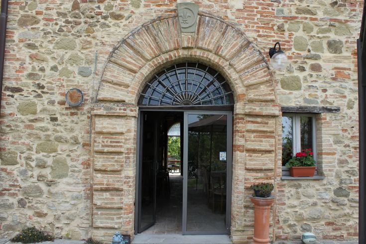 Entrata di un edificio in pietra, caratterizzato da archi semplici e fiori che abbelliscono l'ingresso.