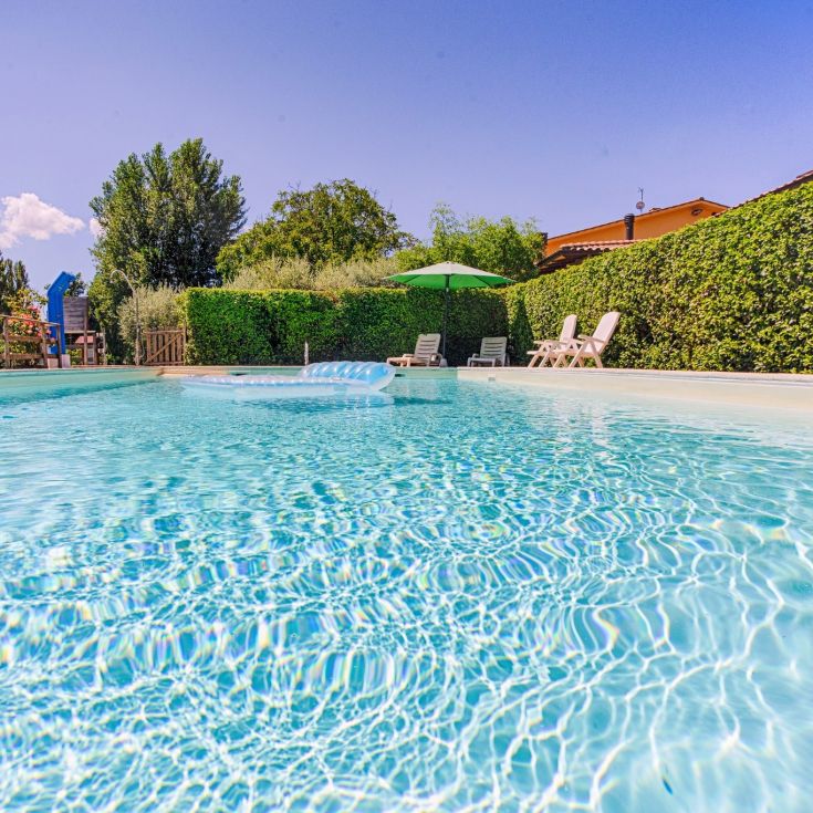 Una piscina chiara circondata da un'area verde di un agriturismo, perfetta per momenti di relax.
