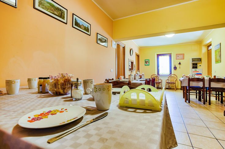 Una semplice sala da pranzo in un agriturismo con tavoli apparecchiati per la colazione.