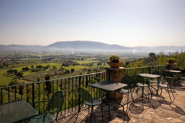 A panoramic view of the Umbrian hills, featuring outdoor iron tables and chairs for a relaxing moment.