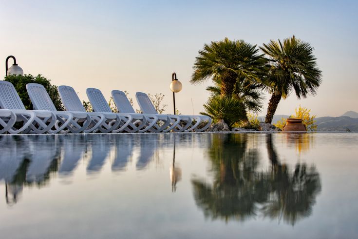 A tranquil pool reflecting palm trees and loungers in a serene sunset landscape.