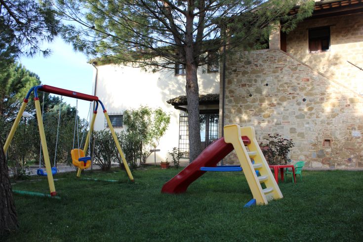 Spazio ricreativo attrezzato per bambini, circondato da verde rigoglioso, perfetto per il gioco all'aperto.