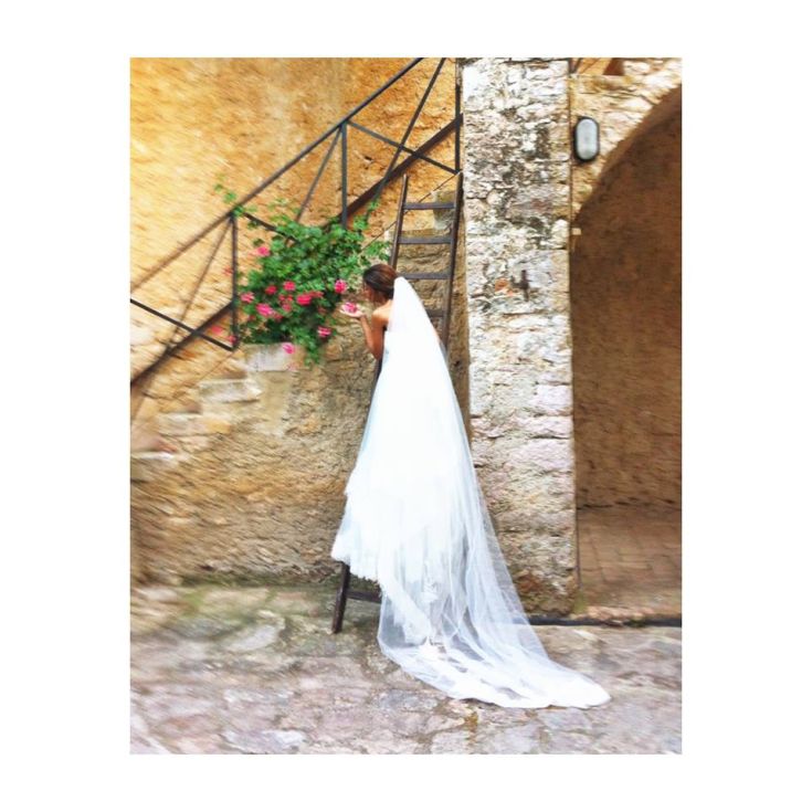 Eine Braut bewundert Blumen, die auf einer Treppe in einer einfachen und bezaubernden Umgebung angeordnet sind.