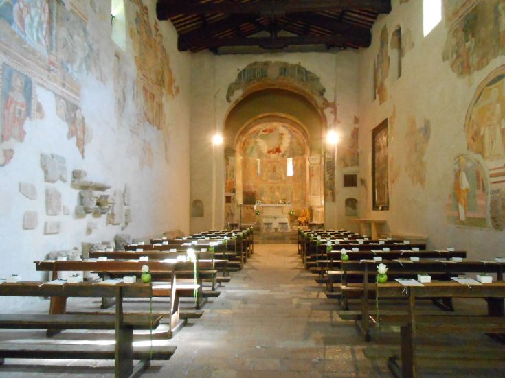Das Innere der Abteikirche mit Fresken und ordentlich angeordneten Holzbänken.