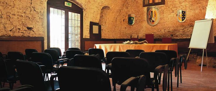 Innenansicht eines Besprechungsraums mit einem rechteckigen Tisch, Stühlen darum herum und Wänden aus grauem Stein.