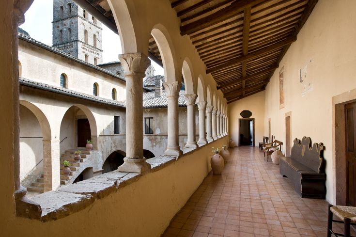 Ein ruhiger Kreuzgang mit Bögen und Säulen, umgeben von einer historischen und natürlichen Umgebung.