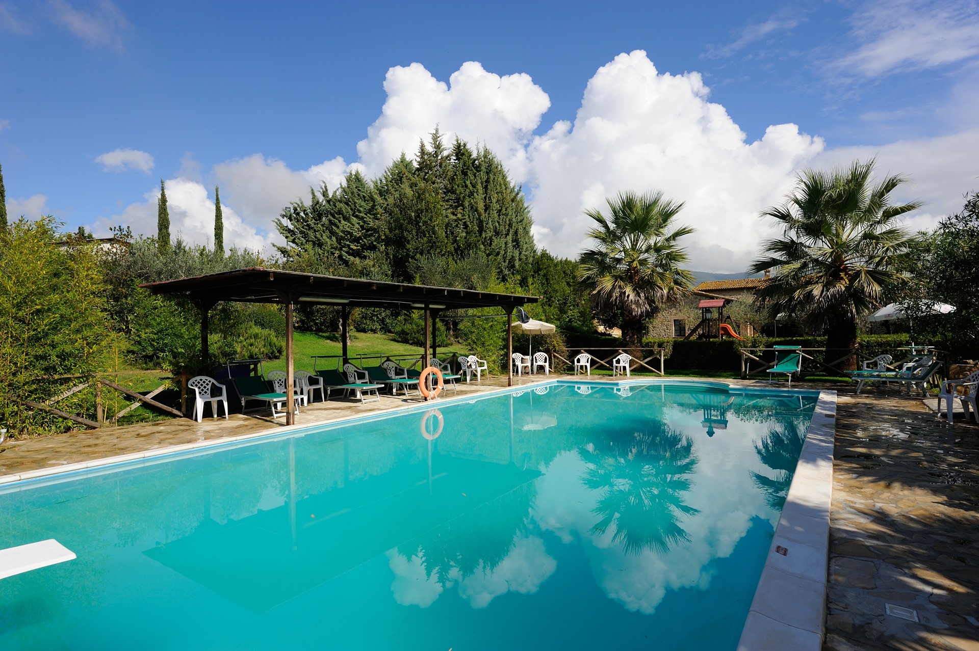 Una piscina situata in un'area verde, circondata da alberi e con un cielo limpido, perfetta per momenti di relax.