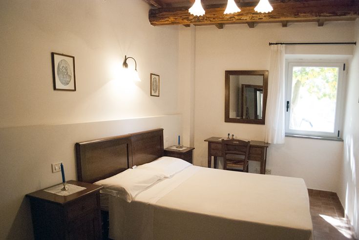 Camera semplice con letto matrimoniale e mobili in legno, situata in un ambiente tranquillo e verde.