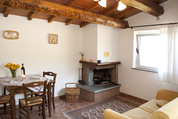 Soggiorno semplice con tavolo, camino e qualche decorazione in stile rustico. Spazio per momenti di relax in Umbria.