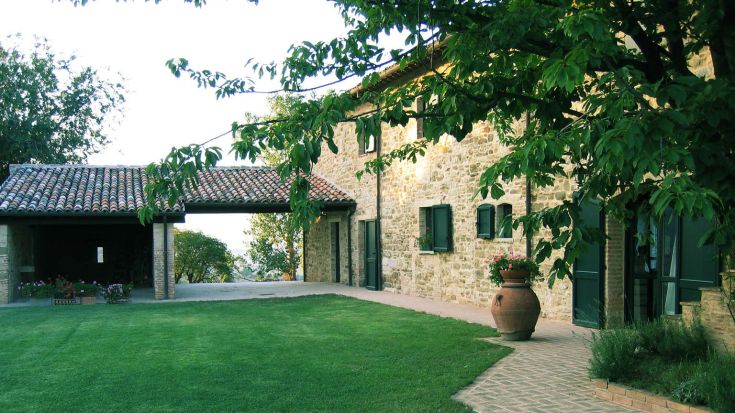Vue d'une ferme avec des façades en pierre et un grand jardin bien entretenu.
