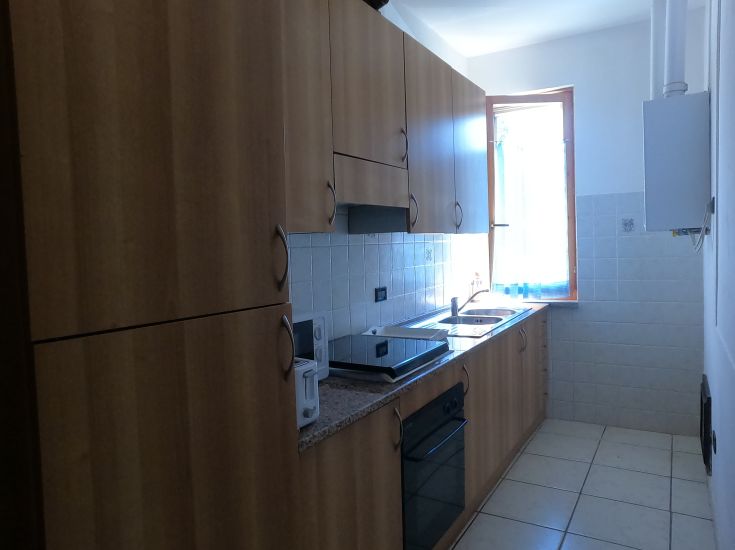 Cucina attrezzata con mobili in legno chiaro, piano cottura, e ampie finestre che portano luce naturale.