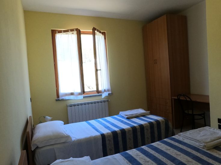 Spaziosa camera di agriturismo con letti singoli e illuminazione naturale, adatta per momenti di relax.