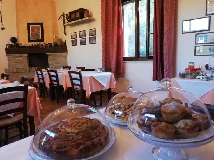 Spazio tranquillo con tavoli ben apparecchiati e dolci freschi sotto cloche, ideale per una colazione serena.