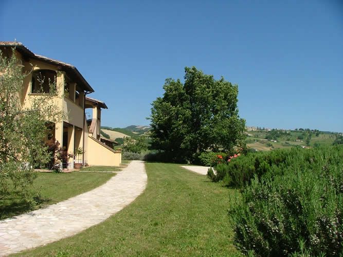 A view of a villa surrounded by greenery, with trees and gentle hills in the background.