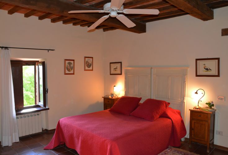 Einfache Schlafzimmer mit Doppelbett, grundlegenden Möbeln und Fenstern mit Blick auf eine grüne Fläche.