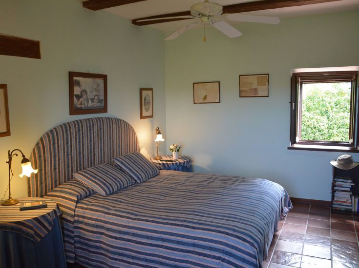 Ein Schlafzimmer mit einem Doppelbett, einfach dekoriert mit Möbelelementen und Blick auf eine grüne Umgebung.