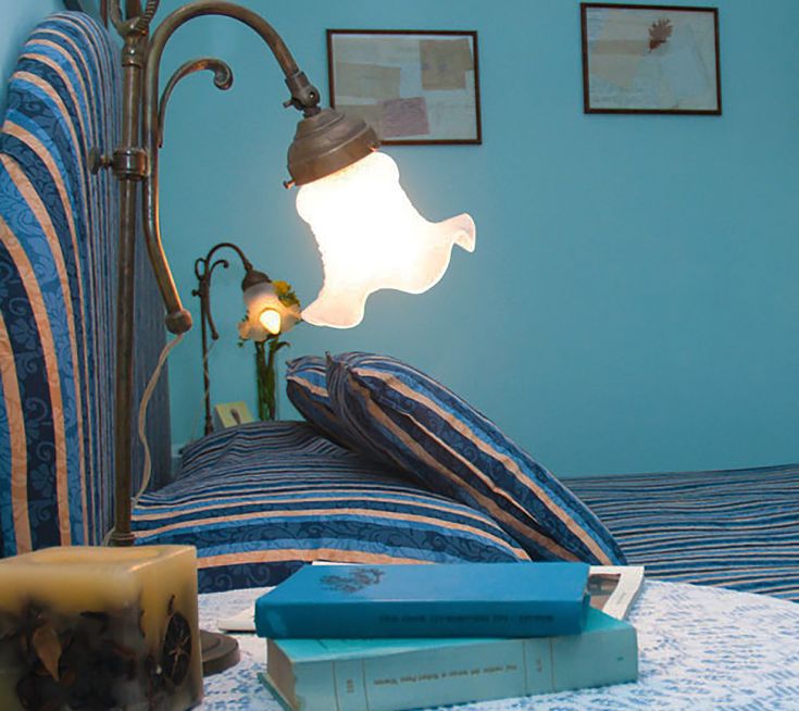 Eine Lampe mit einfachem Design beleuchtet eine gemütliche Ecke mit Büchern und gestreiften Kissen und schafft eine ruhige, entspannte Atmosphäre.