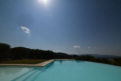 Une magnifique piscine à débordement intégrée dans le paysage, entourée de collines et d'un ciel serein.