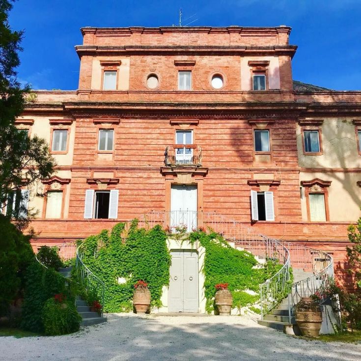 A historic villa surrounded by a lush green garden featuring typical Umbrian plants and flowers.