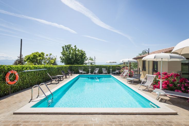 Swimming pool surrounded by umbrellas and sunbeds, located in a green environment for total relaxation.
